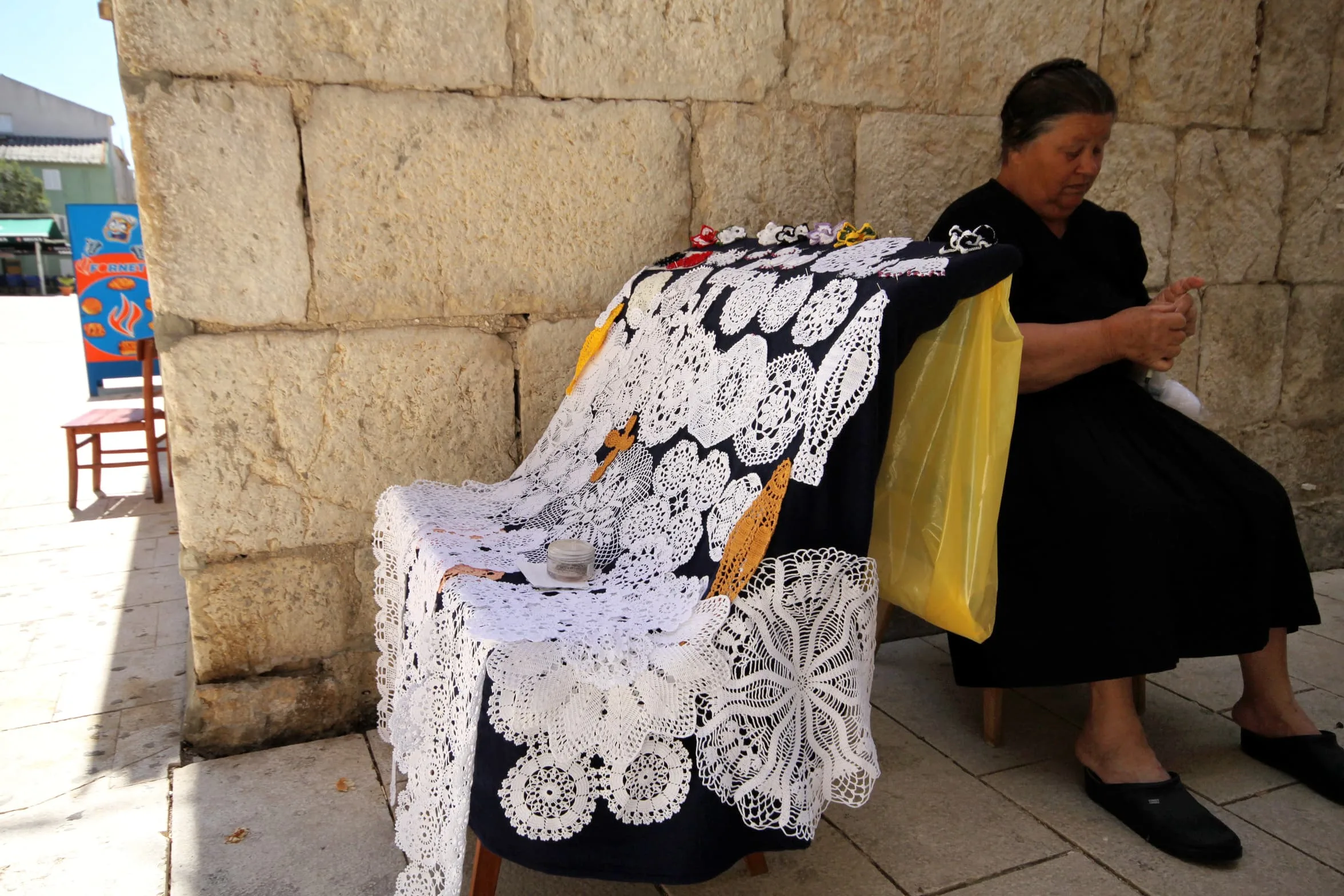 An elderly woman sitting by the wall and knitting authentic Pag lace