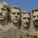 MI által generált fotó a Mount Rushmore szikláról, amerikai elnökök helyett híres horvátok faragott arcával. Luka Modrić, Dražen Petrović, Nikola Tesla és Mate Rimac láthatók, a háttérben a kék ég.