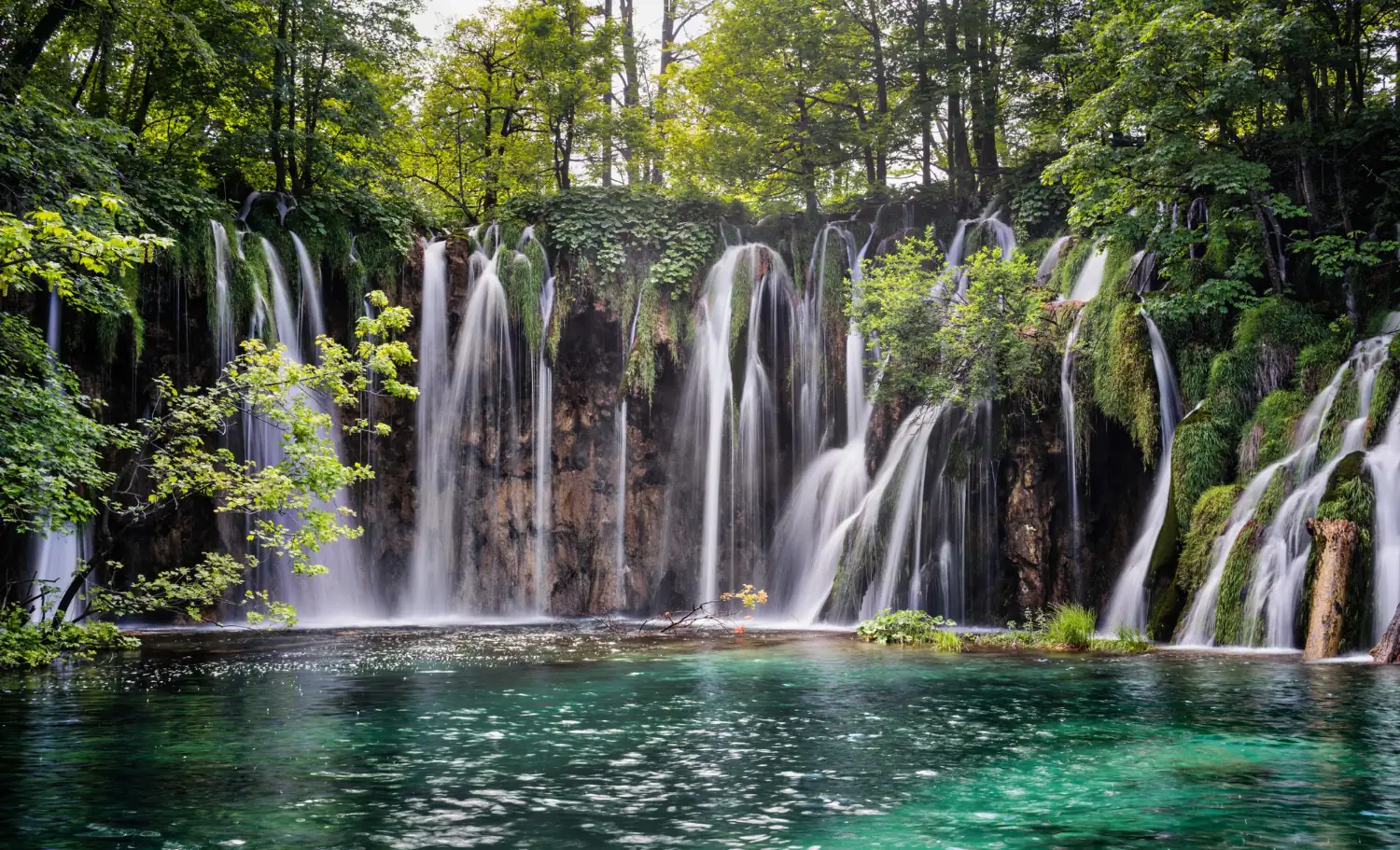 A lake in Plitvice Lakes National Park with waterfalls in the background.
