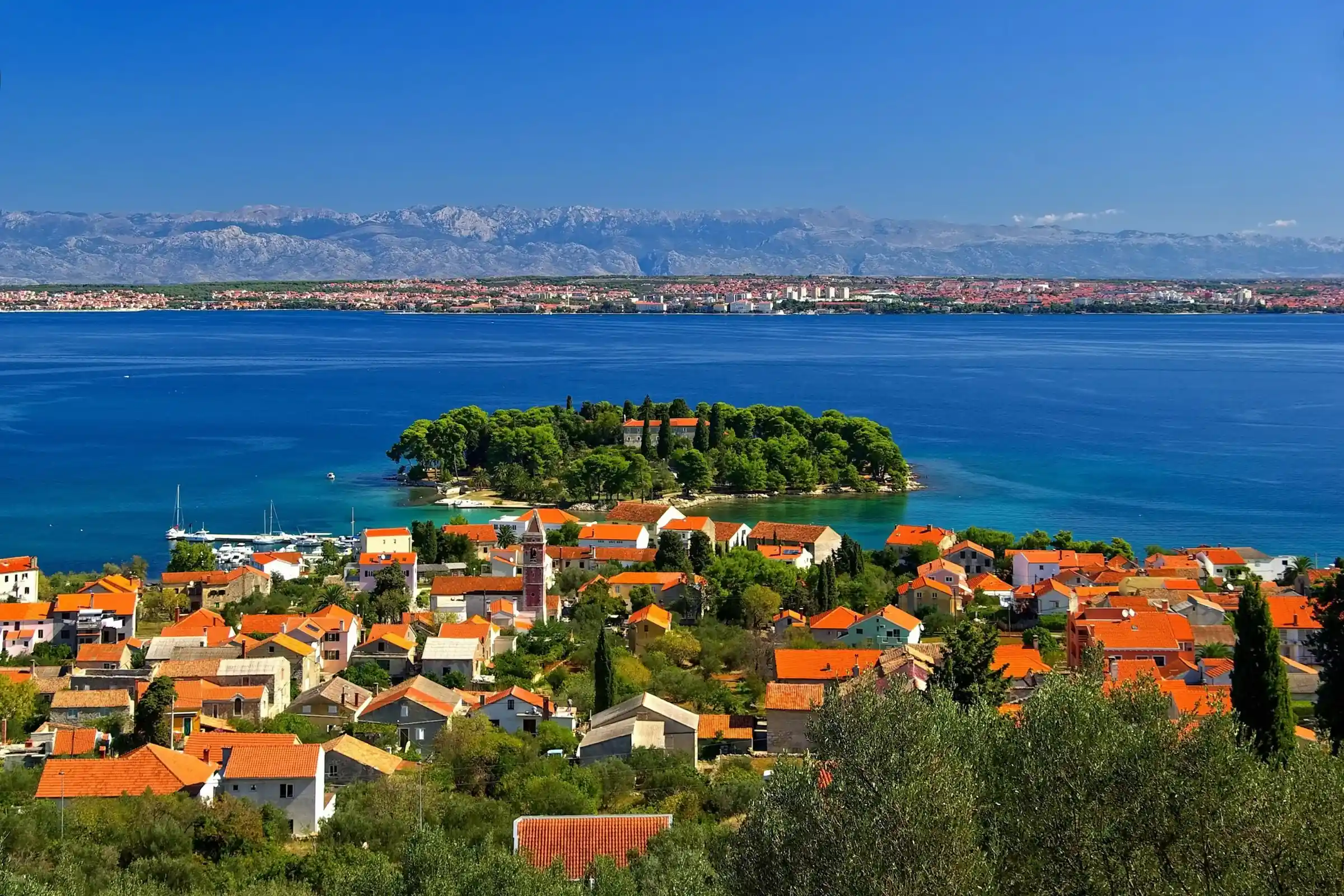 The town of Preko and the islet of Galevac (Školjić) on the island of Ugljan Panoramic view of Preko, the islet of Galevac, and the city of Zadar in the background, on the island of Ugljan.
